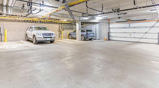A white SUV is parked in a garage with a blue car behind it.