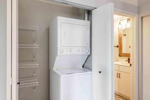 Closet with stacked in unit washer and dryer with shelving and storage.