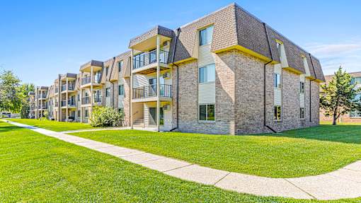 an exterior view of an apartment building with green grass and a sidewalk