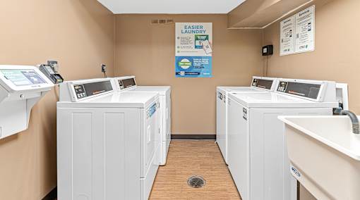 four washers and dryers in a laundry room with two sinks and three was