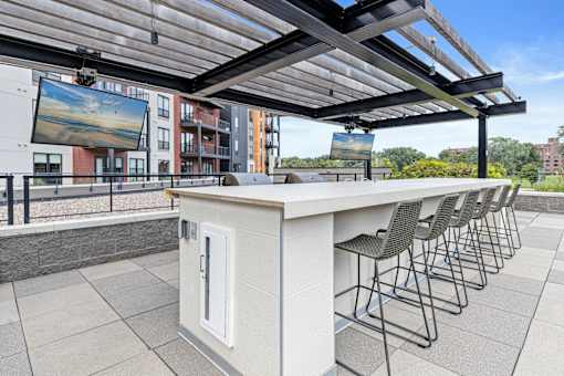 A patio with a bar and chairs under a roof.