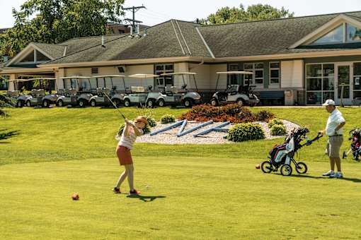 A woman is playing golf in front of a building with several golf carts.