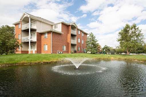 a fountain in the middle of a pond in front of an apartment building