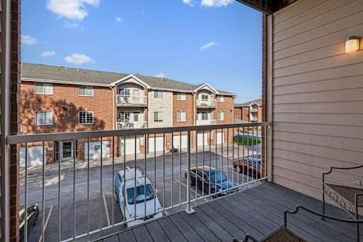 A balcony with a metal railing and a few cars parked in the parking lot.