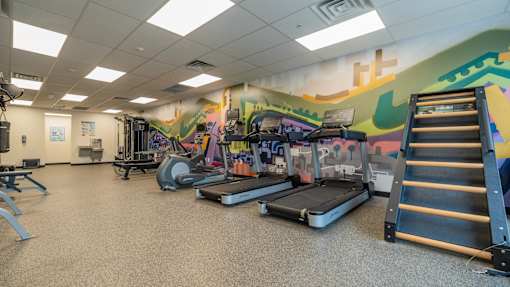 A gym with treadmills, weights, and a wall mural.