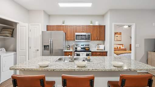 A kitchen with a granite countertop and brown chairs.