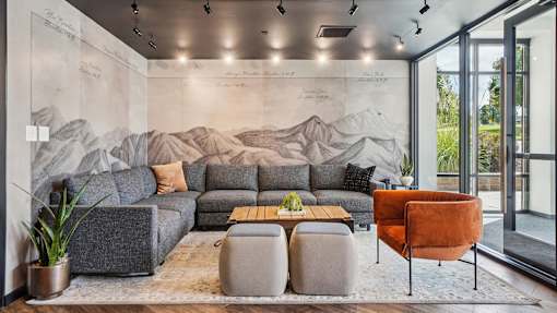 A living room with a grey sofa, a wooden coffee table, and a large mural on the wall.
