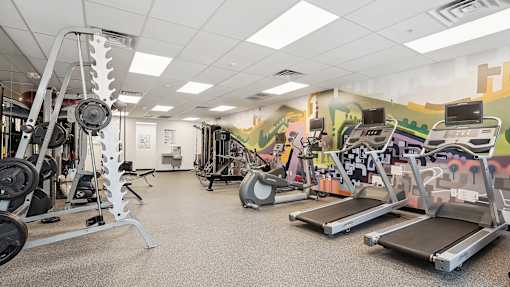 a gym with cardio equipment and a wall with graffiti