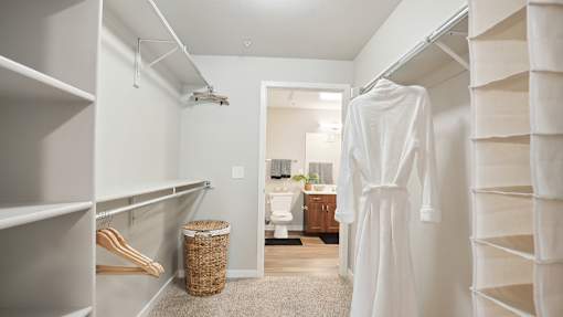 a walk in closet with a white robe and a bathroom