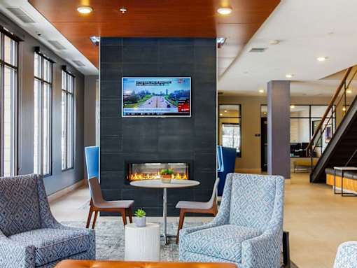 Lobby area with blue lounge chairs, floor to ceiling fireplace with mounted TV above