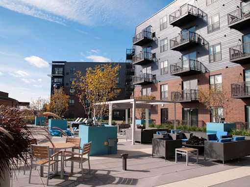 Outdoor community kitchen and lounge area, with tables and couches, balconies in background