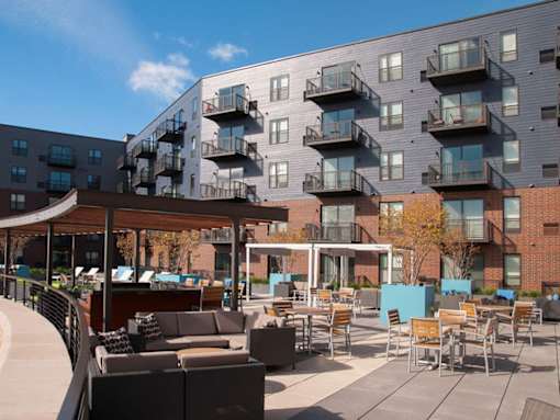 Outdoor community kitchen and lounge area, with tables and couches, balconies in background
