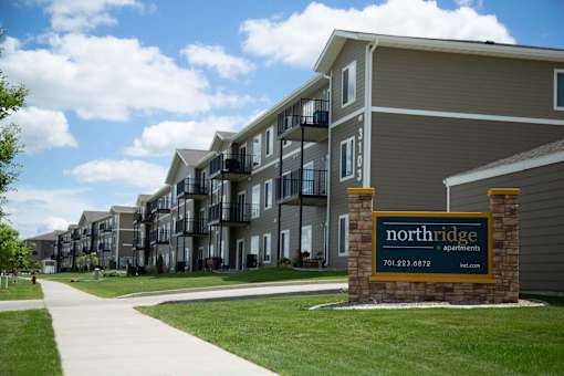 Outside view of Northridge Apartments and the large brick lined sign. Building is gray with white trim and balconies are present on every floor.