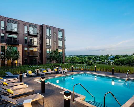 Rooftop pool deck looking out onto green St. Paul grounds. Pool is lined by lights and lounge seating.