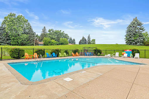 A large outdoor swimming pool surrounded by a fence and lounge chairs.