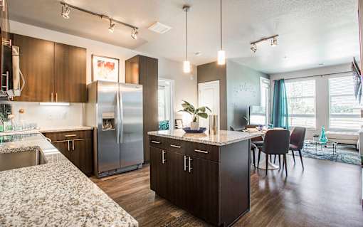 Kitchen open to living room, with dark wood cabinets and granite countertops, central island with overhead lighting