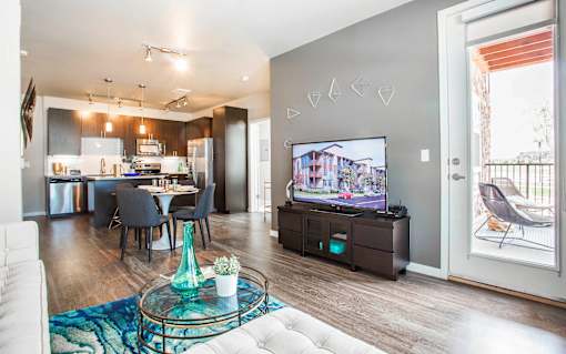 Living room attached to kitchen, with television, sectional couch and door leading to private patio