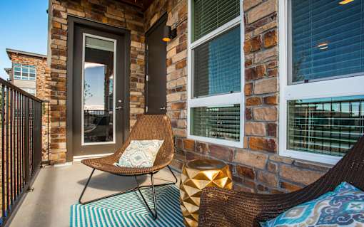 Private balcony with lounge chairs, railing, and door leading into apartment