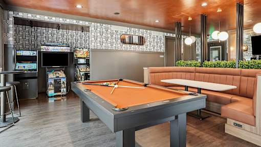 A pool table is in the middle of a room with a bar and arcade games.