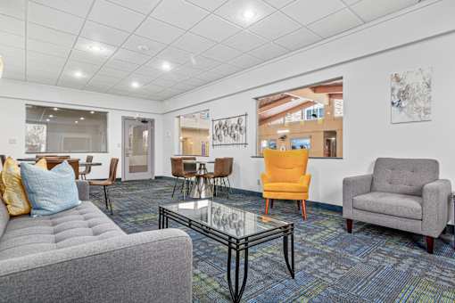 A living room with a grey couch, a yellow chair, a grey armchair, and a glass coffee table.