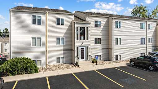 an apartment building with white siding and a parking lot
