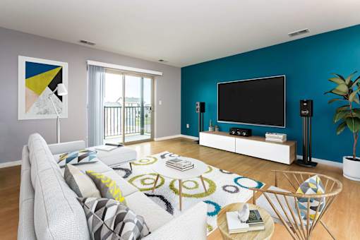 Open and inviting living space with patio doors leading out to private balcony access. TV is wall mounted on the modern accent wall opposite the couch.