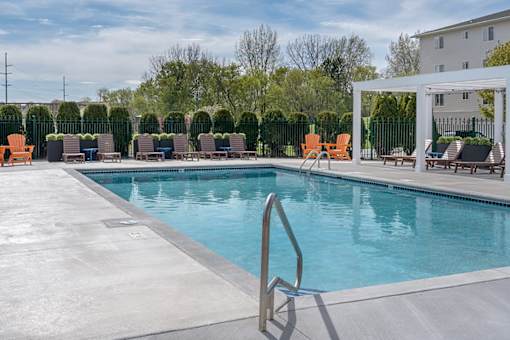 A pool with a metal ladder and chairs around it.