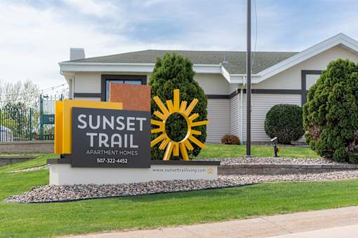 A sign for Sunset Trail Apartment Homes is displayed in front of a building.