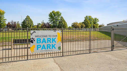 A sign welcoming visitors to Bark Park is displayed on a fence.