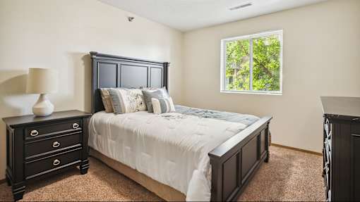 A bedroom with a large bed, a nightstand, and a window.