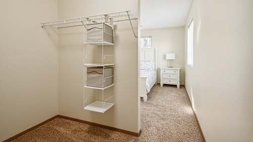 A white bedroom with a bed, nightstand, and a closet with shelves.