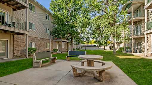 A concrete patio with a picnic table and benches in front of apartment buildings.