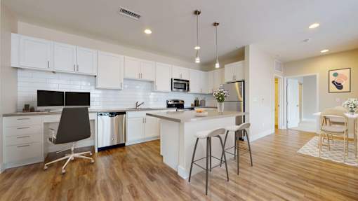 Spacious modern kitchen with white cabinetry, stainless steel appliances, and pendant lighting above the island. Kitchen opens up into separate dining area.