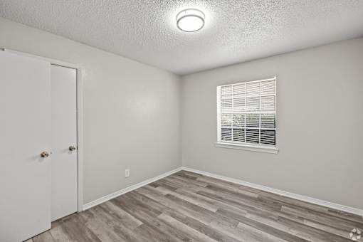 A room with a white door, a window with blinds, and a wooden floor. at La Bella Apartments, Fort Worth, Texas