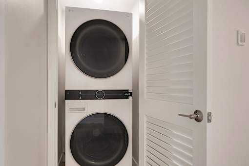 A white door is open to reveal a black washing machine and dryer.