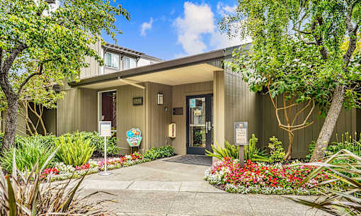 the entrance to a green building with a sidewalk and trees
