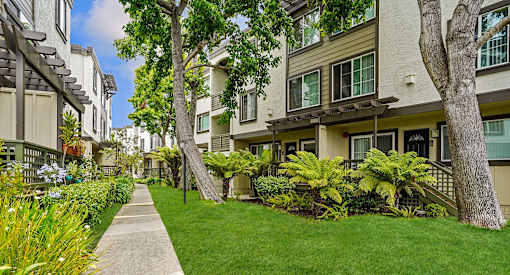 a sidewalk in front of apartments with green grass and trees