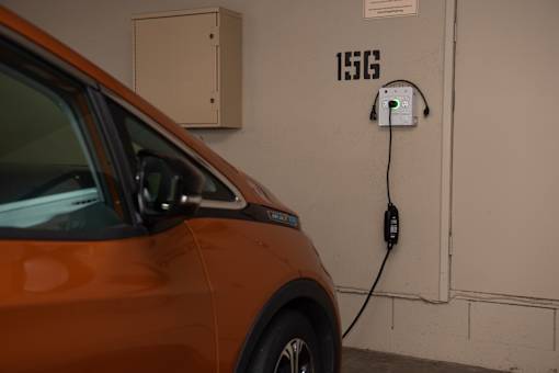 An orange car is plugged into a charging station labeled 156.