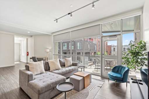 A modern living room with a grey sofa and a glass door leading to a balcony.