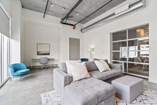 A modern living room with a grey couch, a blue chair, and a white desk.