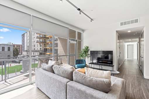 A living room with a grey couch and a balcony with a view of the city.