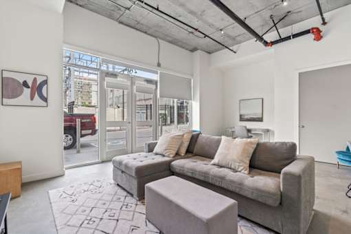 A grey couch with pillows sits in a room with a grey rug and a grey ottoman.