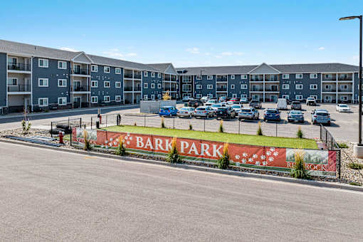 A parking lot in front of apartment buildings with a sign that says Bark Park. at Red Rock Apartments, South Dakota