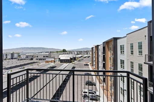 A view from a balcony overlooking a parking lot and a row of buildings.