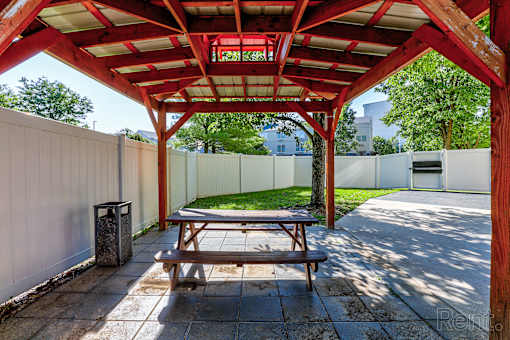 A wooden picnic table is under a red and white canopy.