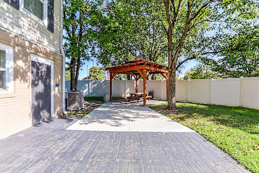 A wooden gazebo is situated in a backyard with a paved walkway leading to it.