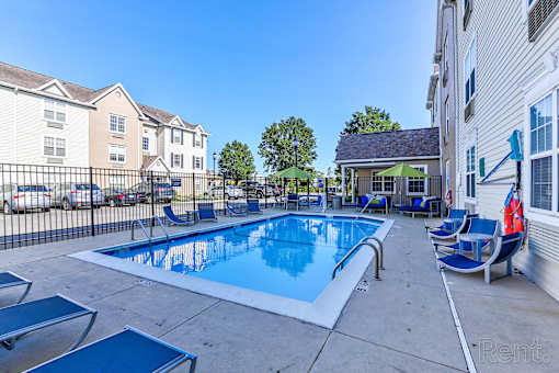 A swimming pool with lounge chairs and umbrellas is surrounded by apartment buildings.