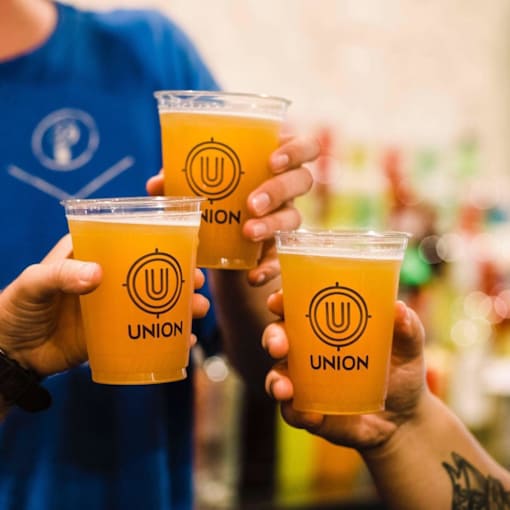 A person holding three cups of Union beer.