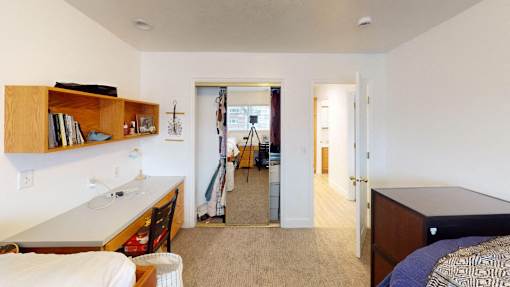 A bedroom with a bed, a desk, and a mirror.
