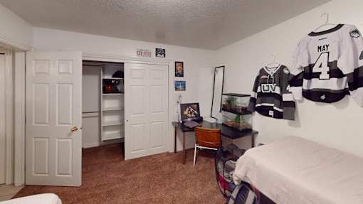 A room with a bed, a chair, a desk, and a hockey jersey hanging on the wall.